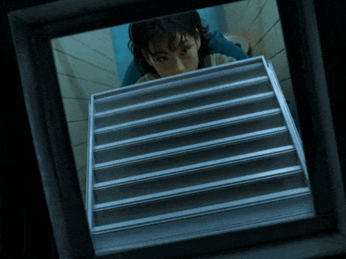a woman in a blue shirt is looking out a window