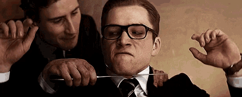 a man with glasses is being cut by another man