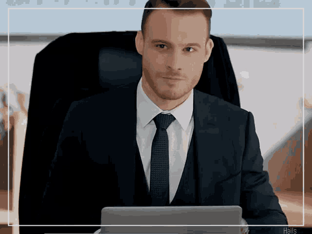 a man in a suit and tie is sitting in front of a laptop computer