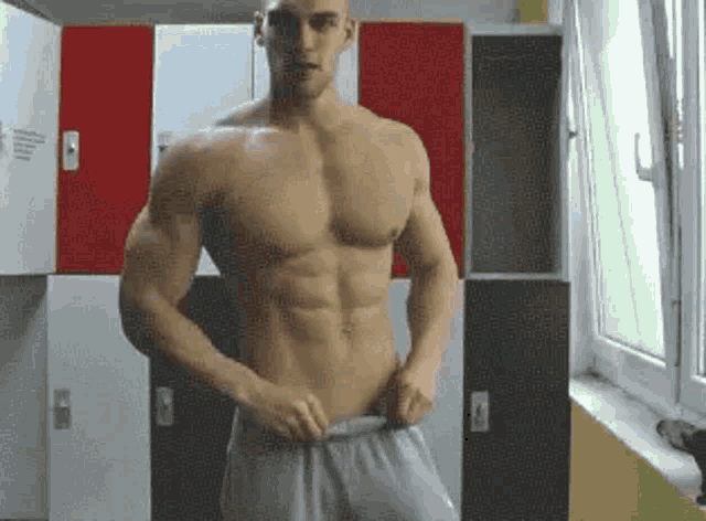 a shirtless man is standing in front of lockers in a gym .
