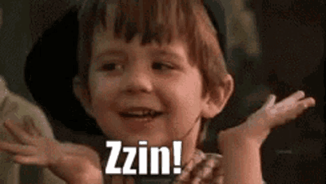 a young boy is smiling and making a funny face with his hands outstretched and the words zzin written on his face .