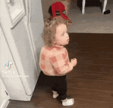 a little girl is standing in front of a refrigerator and making a funny face .