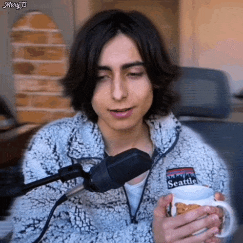 a man wearing a patagonia jacket is holding a cup of coffee in front of a microphone .