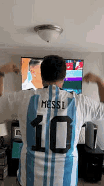 a man wearing a messi 10 jersey is standing in front of a television .