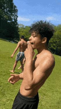 a shirtless man with curly hair is smoking a cigarette in a grassy field