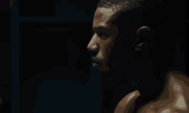 a man without a shirt is standing in a dark room looking at himself in the mirror .