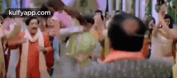 a group of people are dancing in a room with a bald man in the middle .