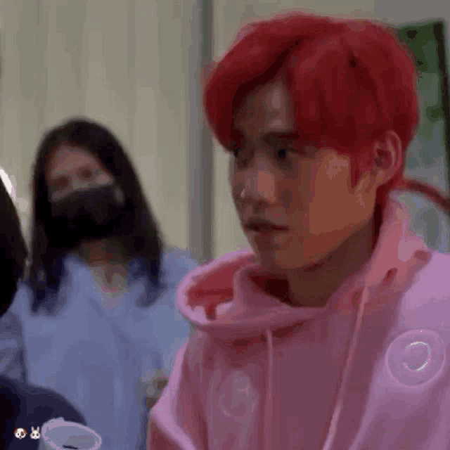 a man with red hair is wearing a pink hoodie and looking at the camera .