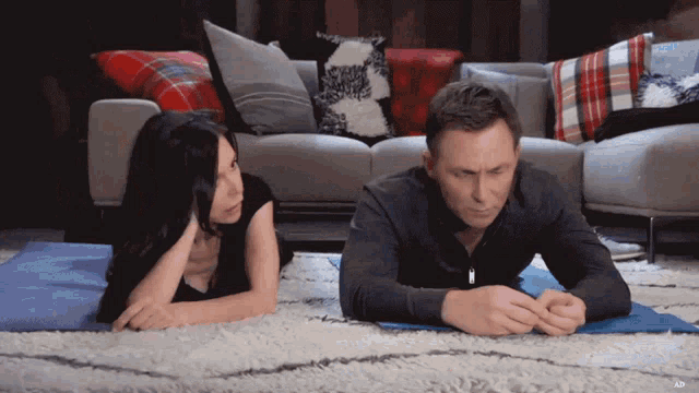 a man and a woman are laying on a yoga mat in front of a couch