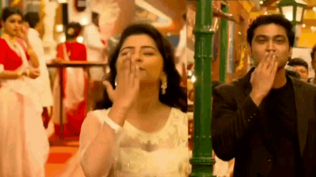 a man and a woman are standing next to each other . the woman is blowing a kiss to the man .