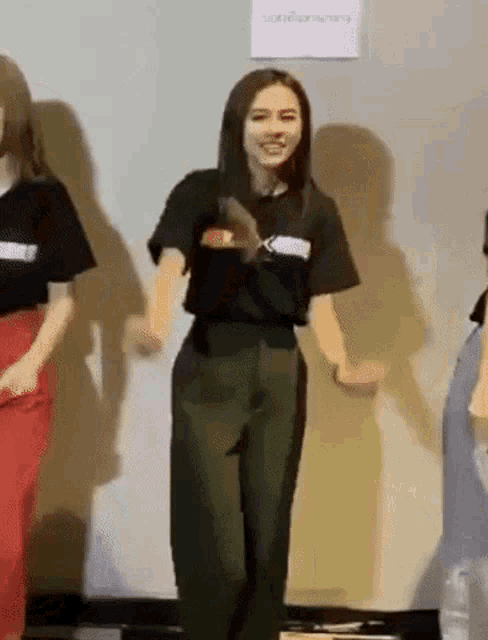 a woman in a black shirt and green pants is dancing in a room with other people .
