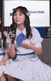a woman in a white dress holds a microphone in front of a screen that says interactive
