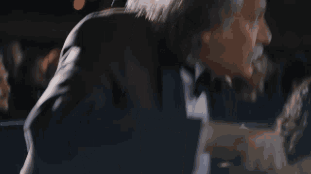 a man in a tuxedo is talking to a woman in a dark room