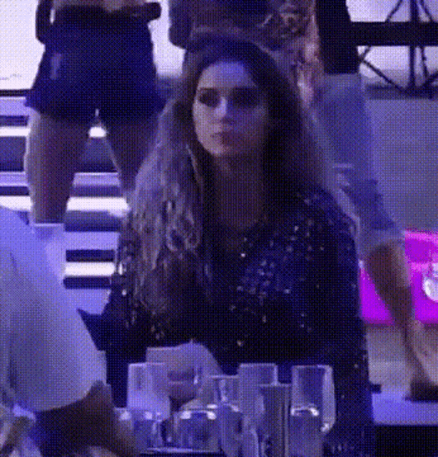 a woman in a sequined dress is sitting at a table with glasses of water .