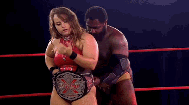 a woman in a red dress is holding a wrestling championship belt in a ring .