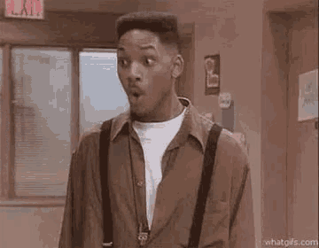 a man with a surprised look on his face is standing in a hallway .