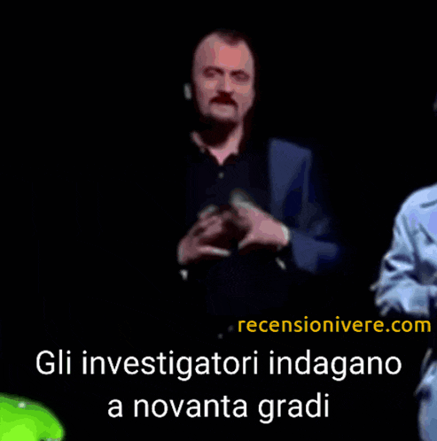 a man with a mustache stands in front of a screen that says gli investigatori indagarno a novata gradi