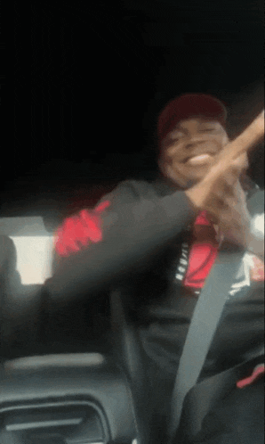 a man in a red hat is sitting in the back seat of a car with his hands in the air .
