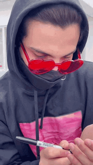 a man wearing a black hoodie and red sunglasses is holding a marker that says sharpie on it