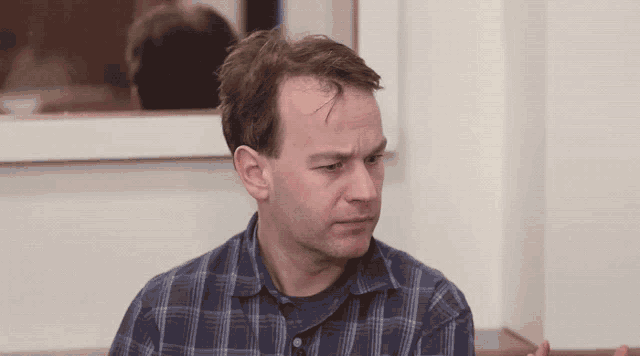 a man wearing a plaid shirt is looking at the camera