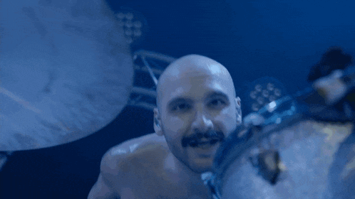 a bald man with a mustache is playing a drum set