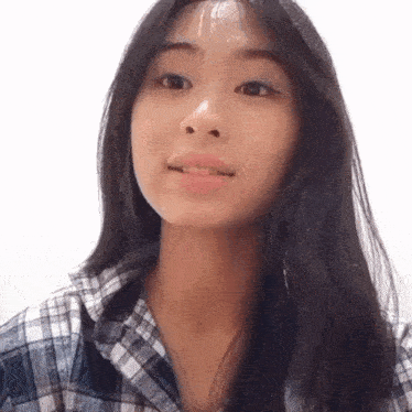 the girl is wearing a plaid shirt and smiling at the camera .