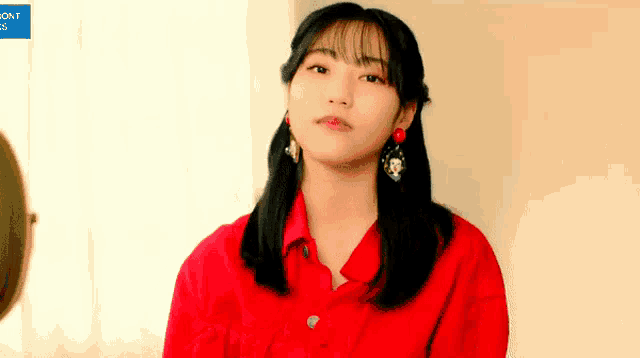 a woman wearing a red shirt and earrings is looking at herself in the mirror .