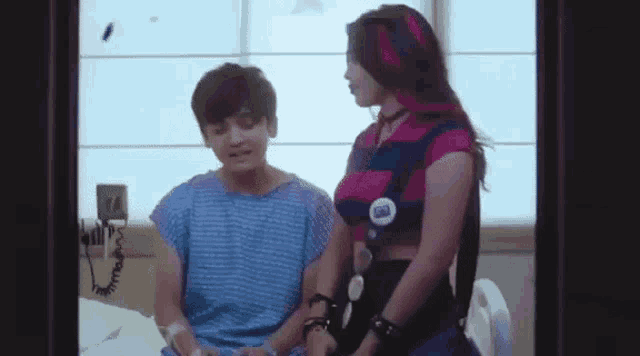 a girl is sitting next to a boy in a hospital bed holding his hand .