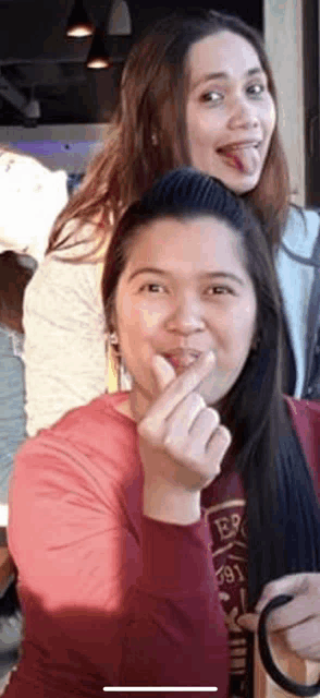 two women are posing for a picture and one of them is making a heart shape with her hand .