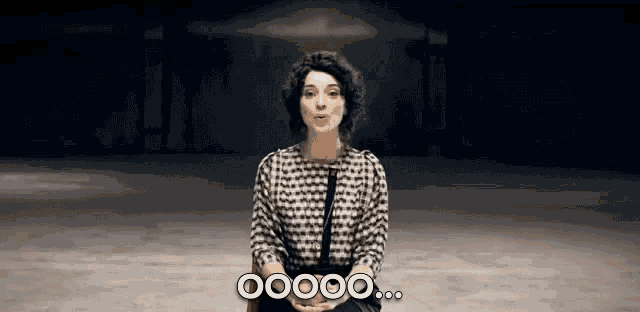 a woman in a black and white shirt is sitting in front of a sign that says ooooo