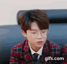a young boy in a plaid jacket and tie is sitting on a couch .