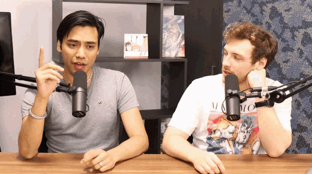 a man in a momo shirt talks into a microphone while another man looks on