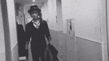 a black and white photo of a man in a fedora walking down a hallway