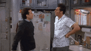 two men are standing next to each other in a kitchen talking .