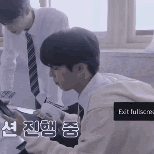 a man in a white shirt and tie looks at a tablet while another man stands behind him