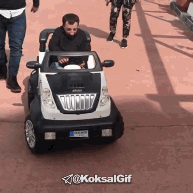 a man is driving a toy car with a license plate that says fatiman on it