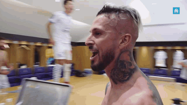 a shirtless man with a tattoo on his neck stands in a dressing room