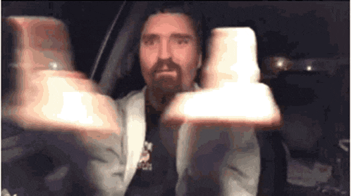 a man with a beard is holding two cups in his hands while sitting in a car .