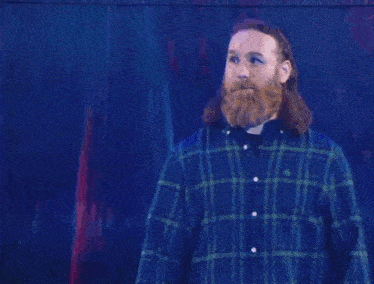 a man with long hair and a beard is wearing a blue plaid shirt