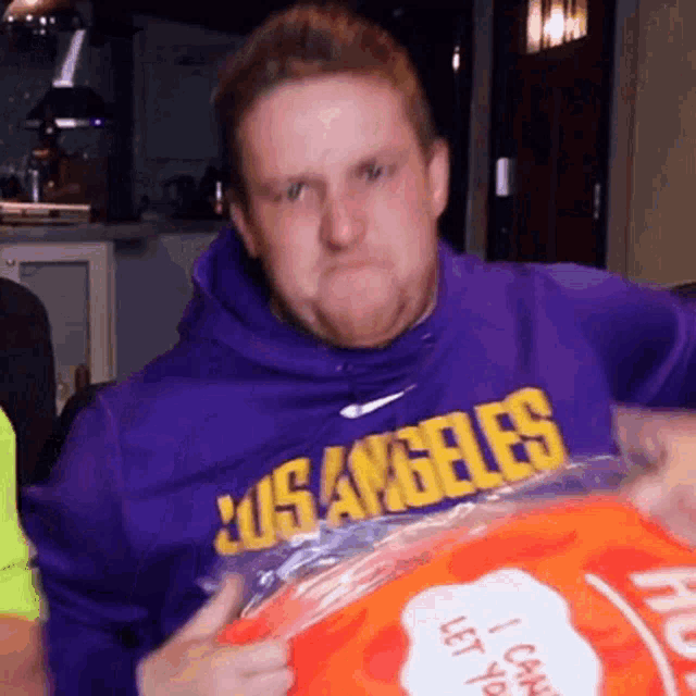 a man wearing a purple los angeles shirt is holding an orange bag
