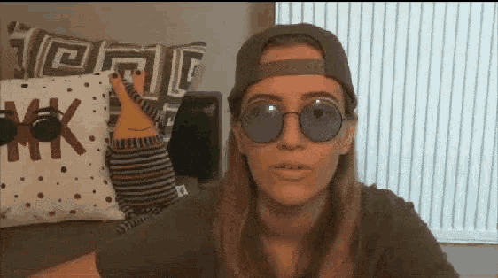 a woman wearing sunglasses and a hat is standing in front of a pillow that says mk