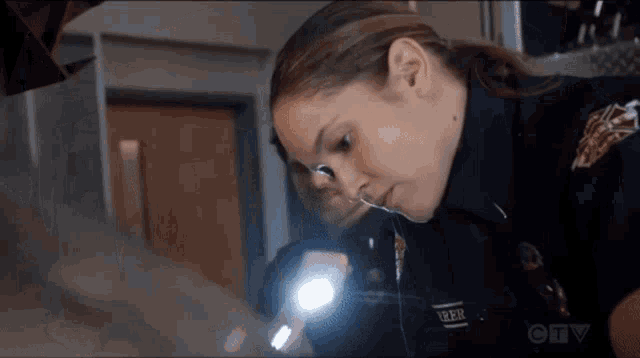 a woman in a police uniform is holding a flashlight and looking at something .