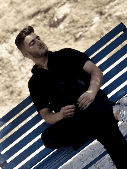 a man in a black shirt is sitting on a blue striped bench