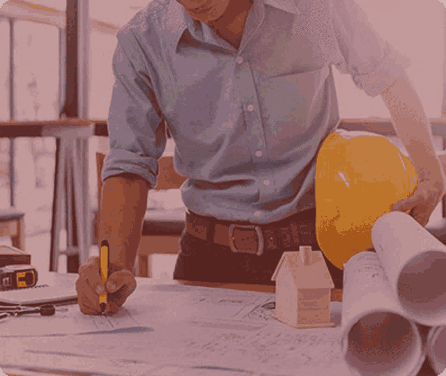 a man wearing a hard hat and a blue shirt is writing on a piece of paper