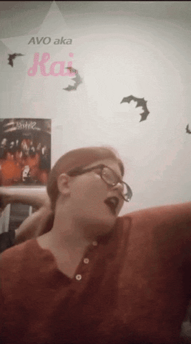 a woman wearing glasses and a red shirt stands in front of a wall with bats and the words avo aka kai on it