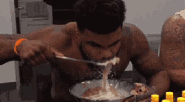 a shirtless man is eating a bowl of soup with a spoon