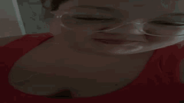 a woman wearing glasses is holding her finger to her nose .