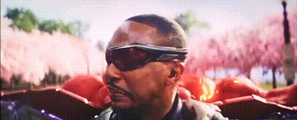 a man wearing sunglasses and a leather jacket is standing in front of a pink background .