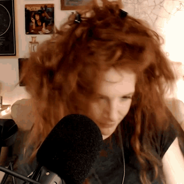 a woman with red hair stands in front of a microphone with a poster on the wall that says pluto