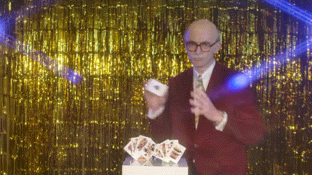 a man in a red suit is holding a stack of playing cards in front of a gold curtain .
